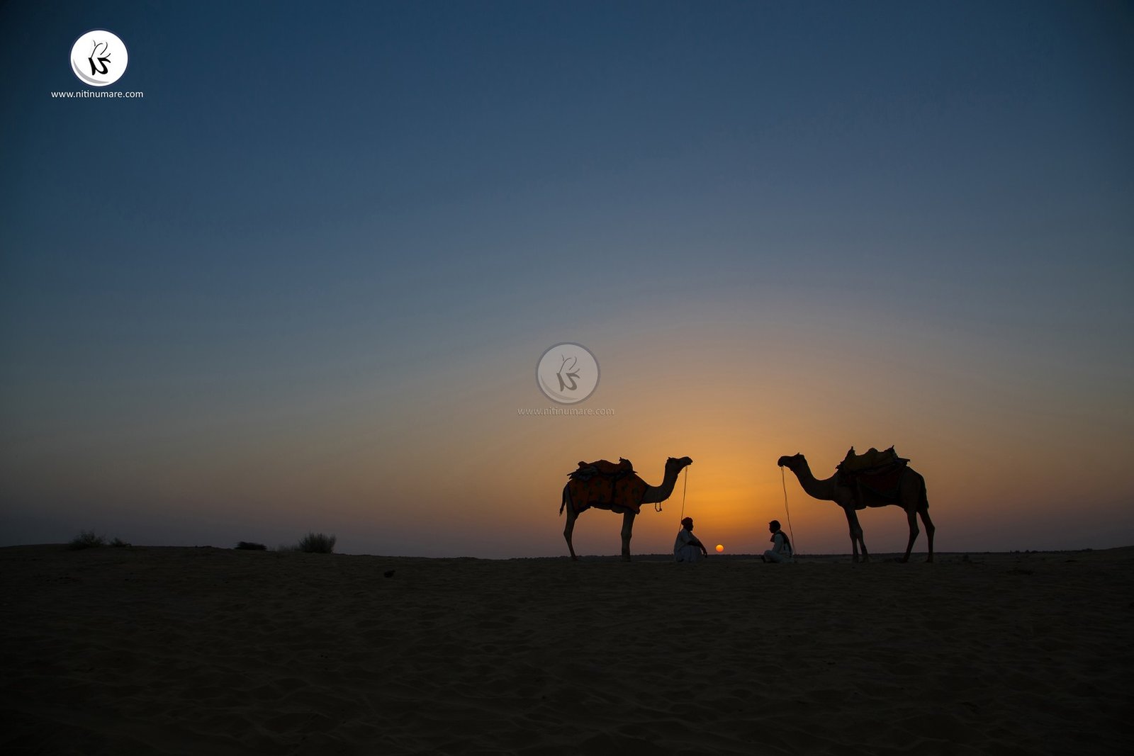 Nice landscape having golden color of sunrise in a blue sky captured with two people and their camels.